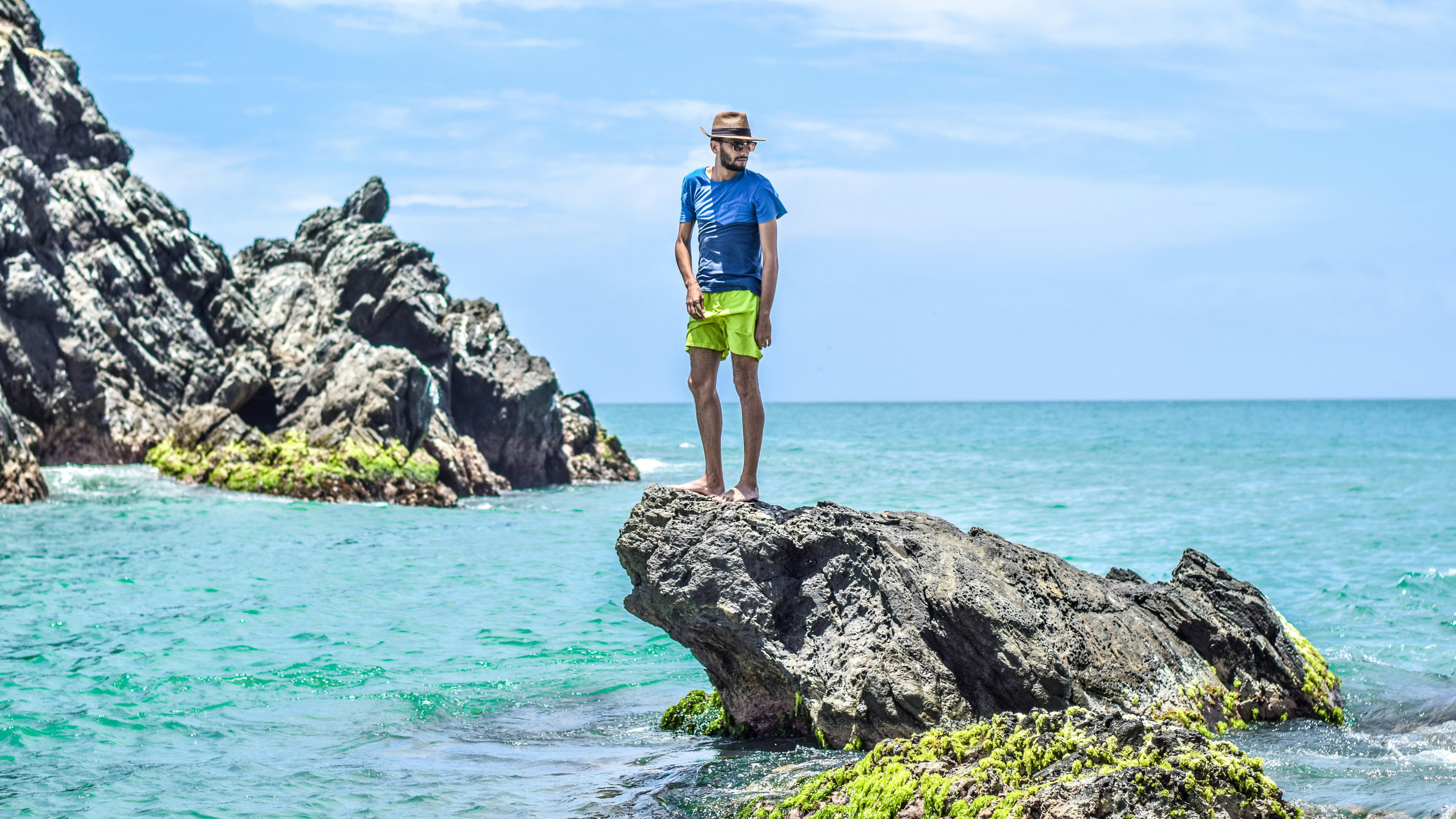 man in blue t-shirt standing on gray rock on see